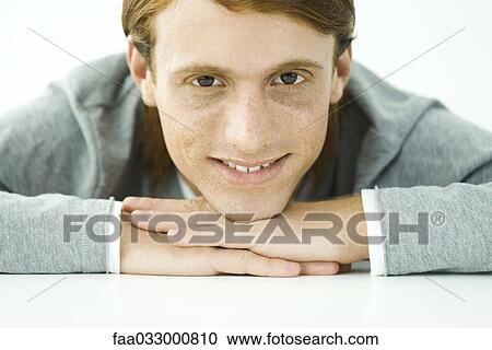 Stock Image - Young man resting head on folded arms, smiling at camera, portrait. Fotosearch
