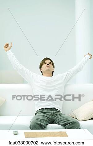 Young man sitting on couch with arms raised View Large Photo Image Stock Image - Young man sitting on couch with arms raised. Fotosearch