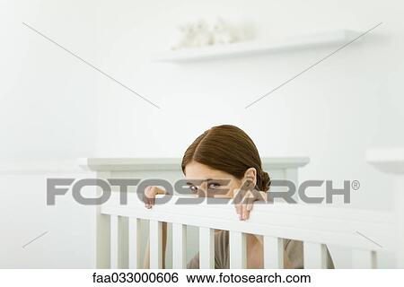 Stock Photograph - Young mother crouching in crib, peeking at camera. Fotosearch