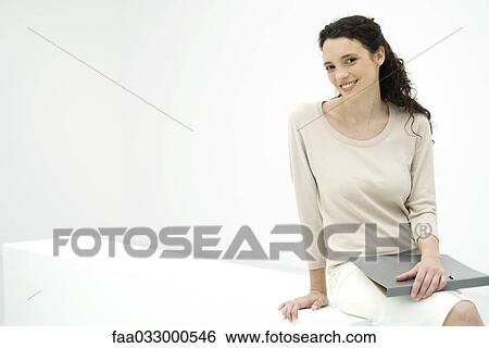 Stock Photograph - Young professional woman holding binder, smiling at camera. Fotosearch