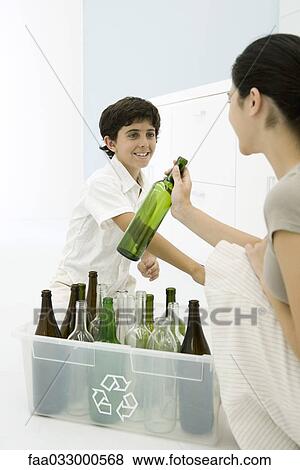 Young woman and boy placing glass bottles in recycling bin, smiling at each other View Large Photo Image Stock Photo - Young woman and boy placing glass bottles in recycling bin, smiling at each other. Fotosearch