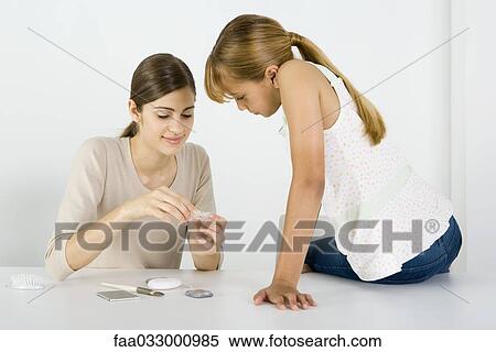 Stock Photography - Young woman and preteen sister looking at cosmetics together, smiling. Fotosearch