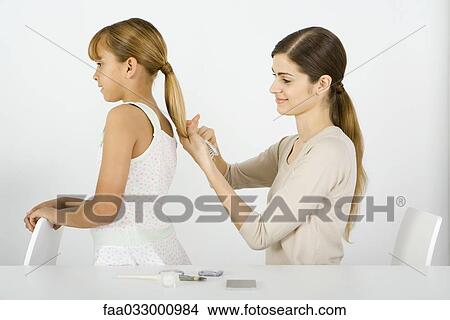 Picture - Young woman combing her younger sister's hair, side view. Fotosearch