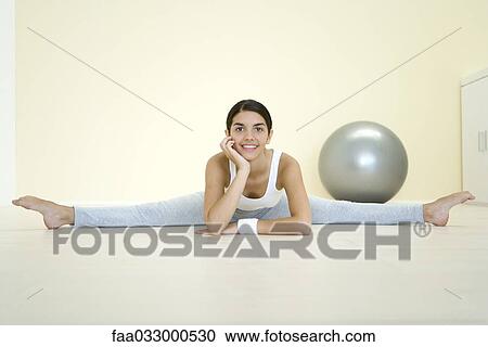 Stock Image - Young woman doing split on the ground, smiling at camera. Fotosearch