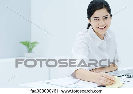 Stock Image - Young woman fidgeting with adhesive notes, smiling at camera. Fotosearch
