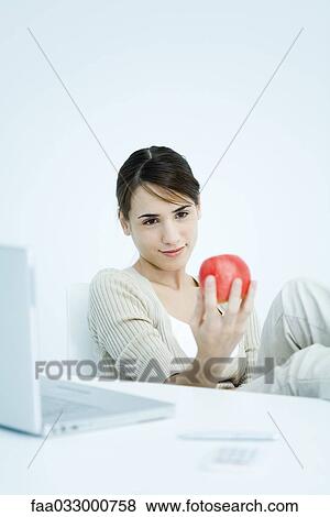 Stock Photo - Young woman holding apple and looking down at it. Fotosearch