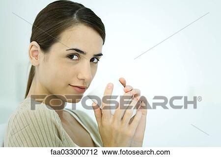 Stock Image - Young woman holding coffee mug, smiling at camera. Fotosearch