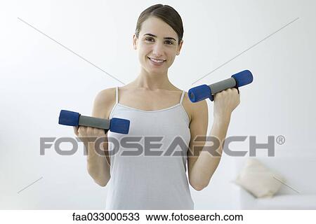 Young woman lifting dumbbells, smiling at camera View Large Photo Image Stock Image - Young woman lifting dumbbells, smiling at camera. Fotosearch