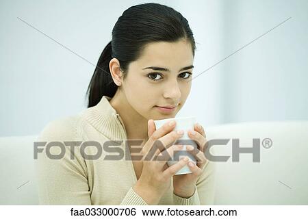 Young woman sitting, holding coffee mug, smiling at camera View Large Photo Image Stock Photograph - Young woman sitting, holding coffee mug, smiling at camera. Fotosearch