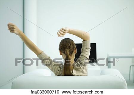 Young woman sitting in armchair, arms outstretched, rear view View Large Photo Image Stock Image - Young woman sitting in armchair, arms outstretched, rear view. Fotosearch