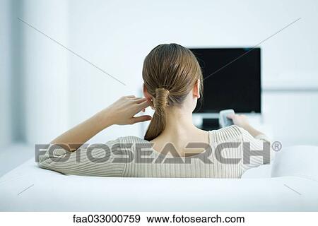 Young woman sitting in armchair watching TV, holding remote, rear view View Large Photo Image Stock Photo - Young woman sitting in armchair watching TV, holding remote, rear view. Fotosearch