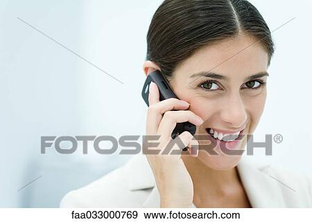 Stock Photo - Young woman talking on cell phone, smiling at camera, portrait. Fotosearch