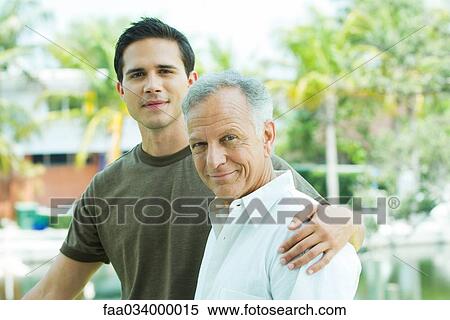Stock Photography - Adult grandson with arm around grandfather, outdoors. Fotosearch
