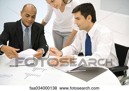 Stock Photo - Associates discussing documents, one man in wheelchair. Fotosearch