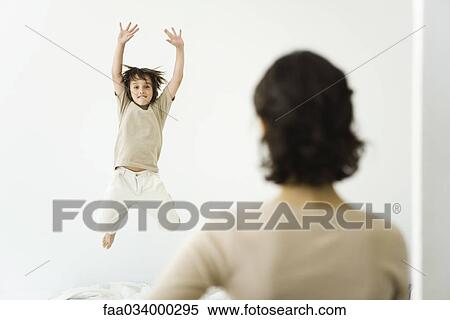 Stock Photography - Boy jumping on bed, mother watching from doorway. Fotosearch