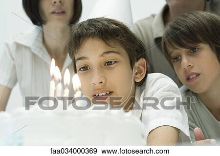 Stock Photo - Boy making a wish before blowing out candles on birthday cake. Fotosearch