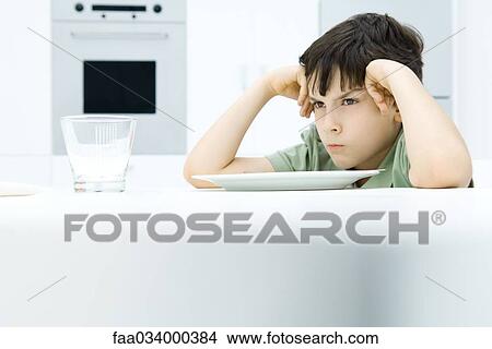 Boy sitting at dinner table, holding head, sulking View Large Photo Image Picture - Boy sitting at dinner table, holding head, sulking. Fotosearch