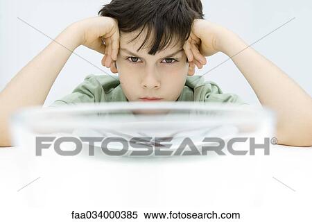 Boy sitting at table, holding head, glaring at camera View Large Photo Image Stock Photography - Boy sitting at table, holding head, glaring at camera. Fotosearch