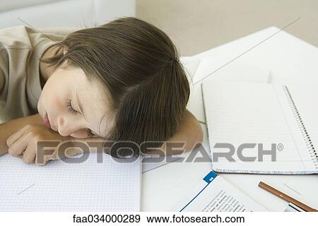 Stock Photo - Boy sitting with homework, head resting on arm, eyes closed. Fotosearch