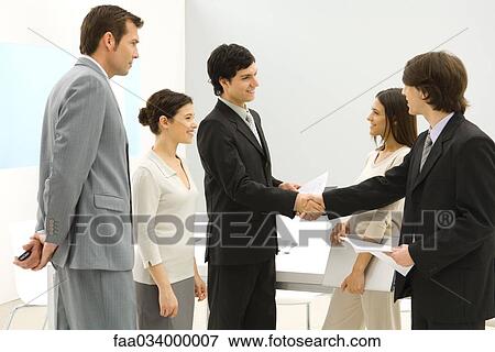 Stock Photo - Business associates meeting, shaking hands while others watch. Fotosearch