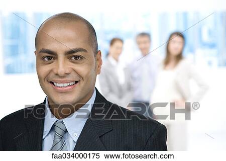 Business executive smiling at camera, colleagues standing in background View Large Photo Image Stock Photography - Business executive smiling at camera, colleagues standing in background. Fotosearch