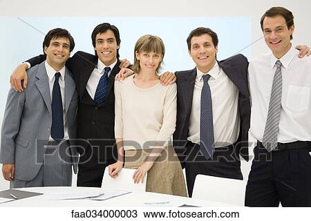 Stock Image - Business team standing with arms around each other's shoulders, smiling at camera. Fotosearch