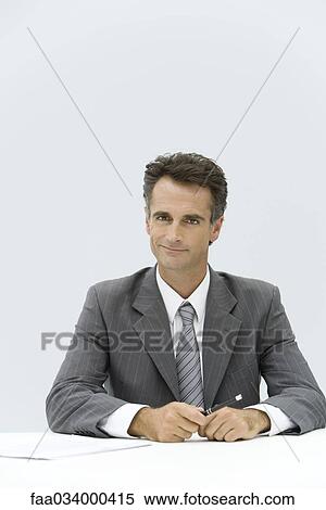 Businessman seated at desk, smiling at camera View Large Photo Image Stock Photography - Businessman seated at desk, smiling at camera. Fotosearch