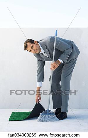 Businessman sweeping, lifting corner of rug, looking at camera View Large Photo Image Stock Photo - Businessman sweeping, lifting corner of rug, looking at camera. Fotosearch