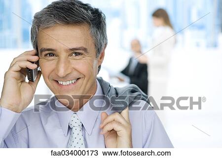 Businessman using cell phone, smiling at camera, jacket slung over shoulder View Large Photo Image Stock Image - Businessman using cell phone, smiling at camera, jacket slung over shoulder. Fotosearch
