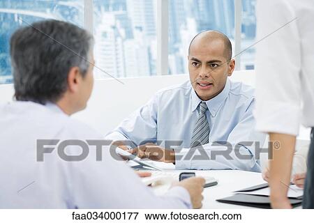 Stock Photo - Businessmen having a meeting at desk, focus on man in background. Fotosearch