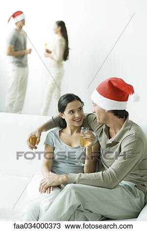 Stock Image - Couple at Christmas party, sitting together on sofa, champagne glasses in hands. Fotosearch