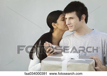 Stock Image - Couple exchanging gifts, woman kissing man on cheek. Fotosearch
