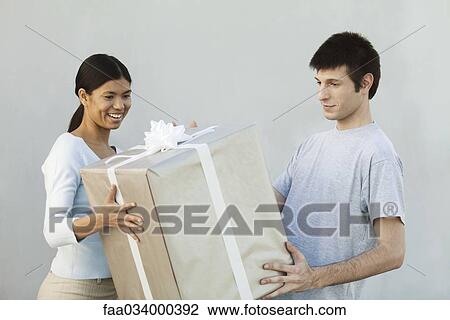 Stock Image - Couple holding large gift together, smiling. Fotosearch