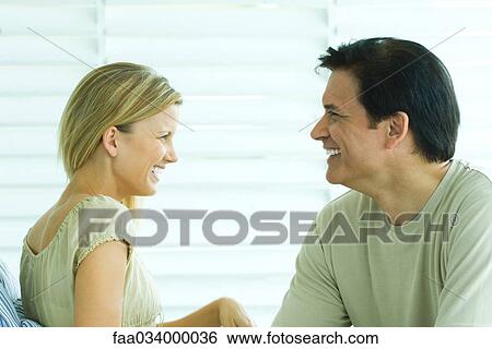 Stock Photograph - Couple sitting together, looking at each other, smiling. Fotosearch