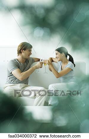 Couple sitting together on sofa, toasting with champagne View Large Photo Image Stock Image - Couple sitting together on sofa, toasting with champagne. Fotosearch