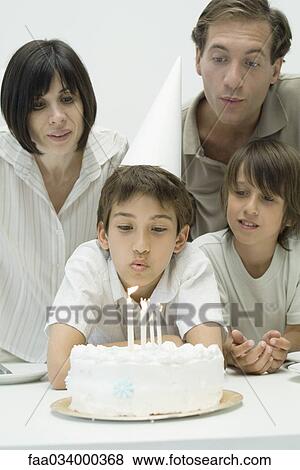 Family watching boy blow out candles on birthday cake View Large Photo Image Stock Photo - Family watching boy blow out candles on birthday cake. Fotosearch