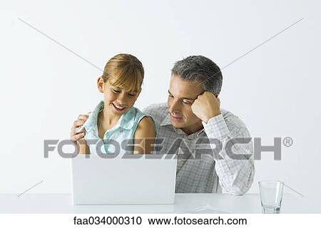Stock Image - Father and daughter looking at laptop computer together, both smiling. Fotosearch