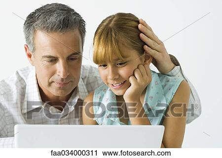 Stock Image - Father and daughter looking at laptop computer together, man's hand on girl's head. Fotosearch
