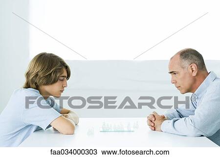 Stock Image - Father and teen son playing chess, side view. Fotosearch