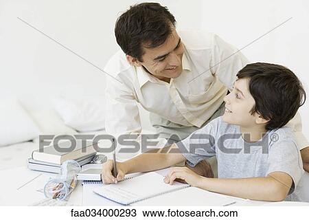 Stock Image - Father helping son with homework, both smiling at each other. Fotosearch
