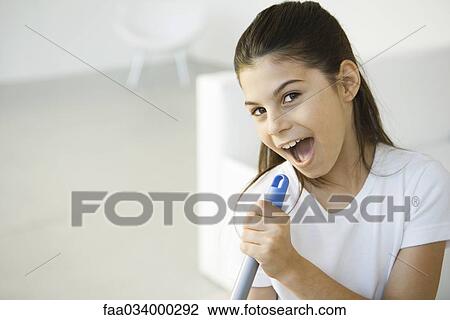 Stock Image - Girl holding broom handle, pretending to sing into microphone. Fotosearch