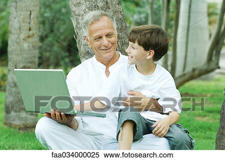 Stock Photography - Grandfather holding grandson on lap, boy looking at laptop computer, both smiling. Fotosearch