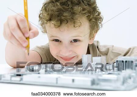 Stock Photo - Little boy holding pencil over computer motherboard, smiling at camera. Fotosearch