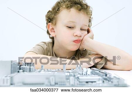 Stock Photo - Little boy leaning on elbow, contemplating computer motherboard. Fotosearch