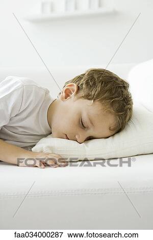 Stock Photo - Little boy napping on bed, eyes closed. Fotosearch