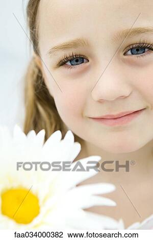 Stock Image - Little girl holding daisy, smiling, portrait. Fotosearch