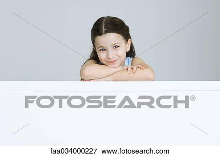 Stock Photo - Little girl resting head on arms, smiling, portrait. Fotosearch