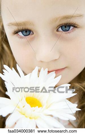 Stock Image - Little girl with blue eyes holding daisy, portrait, close-up. Fotosearch