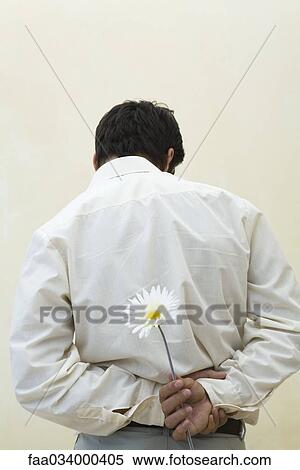 Stock Photography - Man holding flower behind his back, rear view. Fotosearch