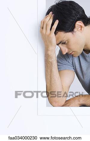 Stock Image - Man holding head, looking down, portrait. Fotosearch